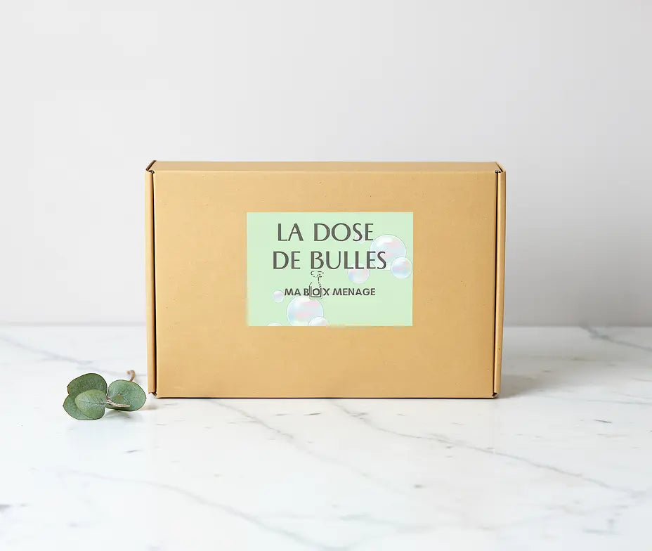 Boîte kraft simple surTableau blanc, étiquette pastel “La Dose de Bulles” au centre, produit ménager naturel sans abonnement.