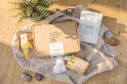 Boîte cadeau éco-nettoyants: carton "La Dose de Bulles" entouré d'accessoires naturels sur lin beige et plantes vertes.